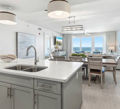 Your modern kitchen island seamlessly flows into the dining area, where ocean views stretch endlessly beyond elegant furnishings.