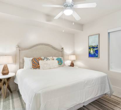 Sink into coastal comfort with crisp white linens, cheerful throw pillows, and a gentle ceiling fan to keep you cool.