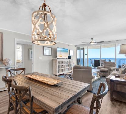 Picture yourself unwinding in this coastal-chic space, where natural light flows through floor-to-ceiling windows framing stunning gulf views. The open layout invites you to gather around the rustic dining table or sink into plush seating.