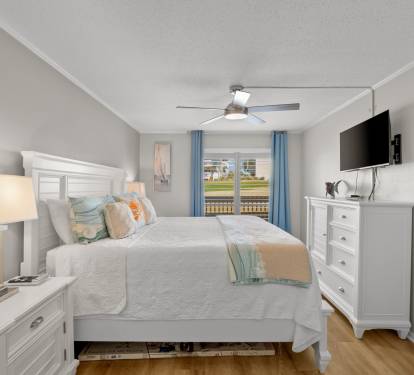 This inviting primary bedroom features a comfortable king bed, coastal-inspired furnishings, and relaxing golf course views just outside. A peaceful retreat designed for comfort, relaxation, and restful nights.