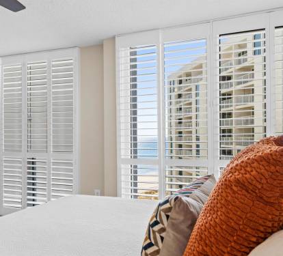 Wake up in this bright bedroom where white shutters frame stunning city views and soft linens invite restful sleep.