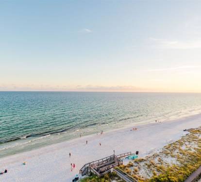 Beautiful Gulf Coast beach with pristine white sand and emerald waters stretches along the shoreline during golden hour.