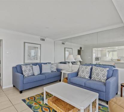 Relax in your spacious living room with comfortable blue sofas and elegant coastal decor, flowing seamlessly into the modern kitchen.