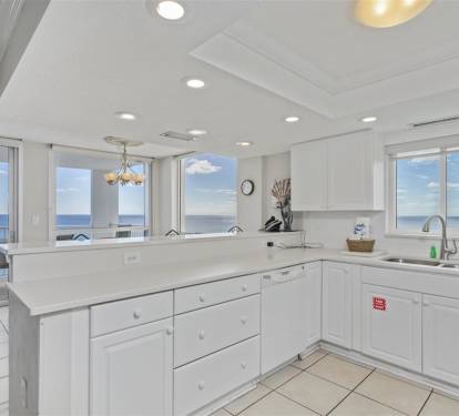 Cook with breathtaking ocean views through floor-to-ceiling windows in your fully equipped kitchen with white cabinetry and modern appliances.