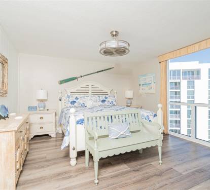 Your coastal bedroom features nautical charm with ocean-inspired bedding and expansive city views through floor-to-ceiling windows.