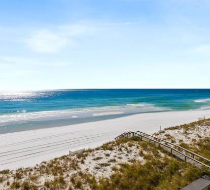 Pristine white sand beach stretches along turquoise waters, with wooden boardwalk leading through coastal dunes.