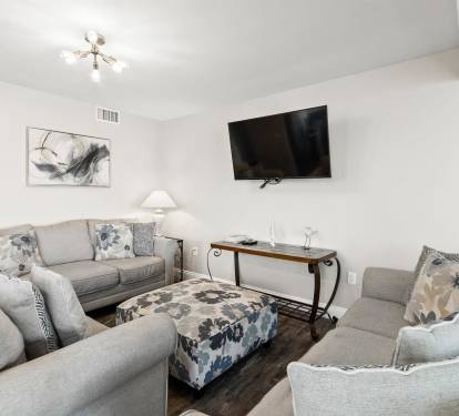 Relax in your spacious living room with plush gray seating, modern entertainment center, and elegant décor creating the perfect retreat.