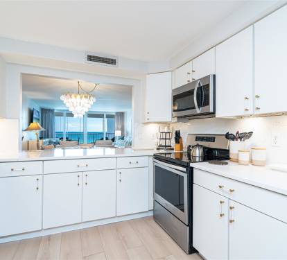 Your elegant kitchen opens to breathtaking ocean views, featuring modern appliances and pristine white cabinetry perfect for preparing memorable meals.
