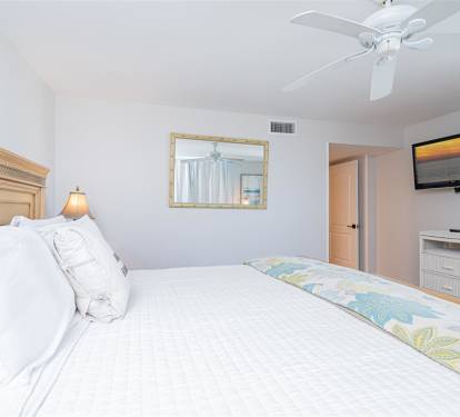 Sink into plush white linens and drift off as your ceiling fan creates a gentle breeze in this serene bedroom retreat.
