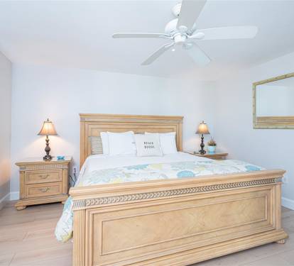 Sink into crisp linens and coastal comfort in your serene bedroom, where gentle ceiling fan breezes and warm bedside lighting create perfect relaxation.