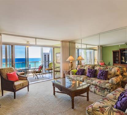 Step into your tropical living room where plush floral seating meets stunning ocean views through floor-to-ceiling windows.