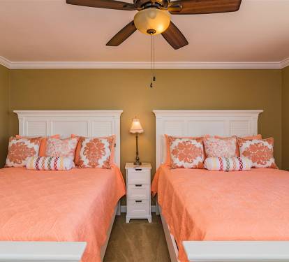 Rest peacefully in your cozy twin bedroom with cheerful coral bedding and warm lighting that creates the perfect atmosphere for a good night's sleep.