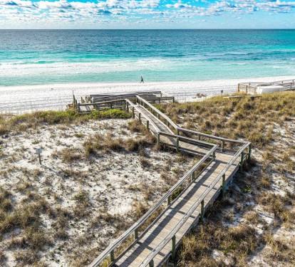Pristine white sand beach with wooden boardwalk leading to turquoise waters and endless ocean views.