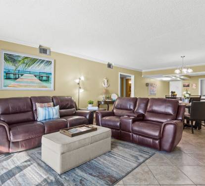 Relax in your spacious living room with plush leather recliners and tropical artwork creating the perfect coastal retreat atmosphere.