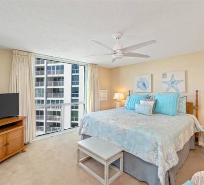 Relax in your serene coastal bedroom with aqua linens, warm lighting, and city views through floor-to-ceiling windows.