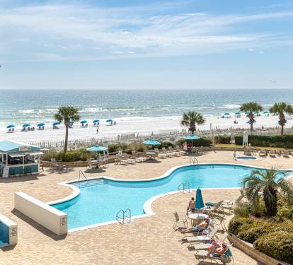 Oceanfront property overlooking a pristine beach and sparkling pool area with palm trees and sandy shores.