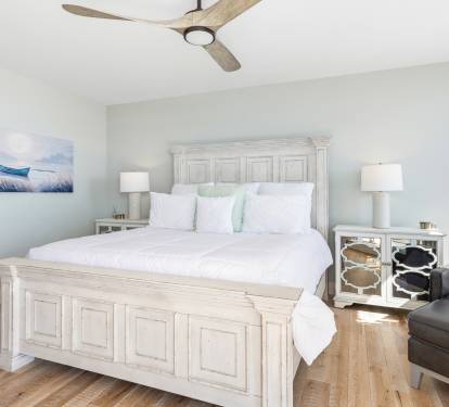 Sink into crisp white linens and coastal charm in your serene bedroom, where gentle sea breezes from the ceiling fan ensure restful nights.
