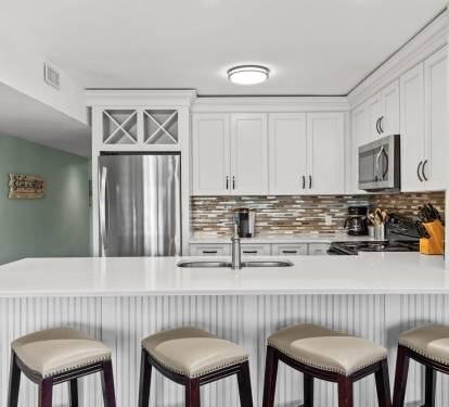 Beautifully updated coastal kitchen with quartz-style countertops, stainless steel appliances, and bar seating perfect for casual dining, morning coffee, or gathering after the beach.