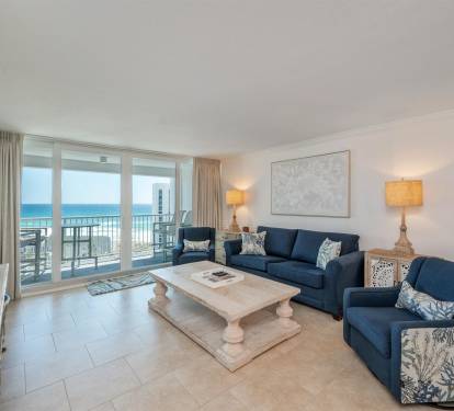 Relax in your spacious oceanfront living room with stunning sea views through floor-to-ceiling windows and comfortable coastal-themed seating.