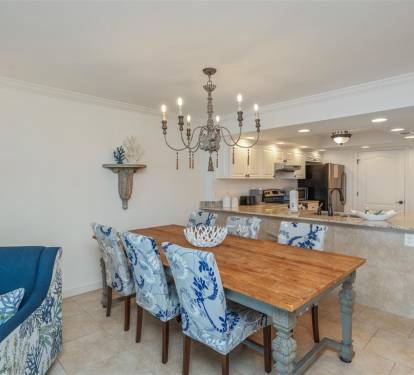 Gather around your coastal dining table for memorable meals beneath an elegant chandelier, with the open kitchen ready for easy meal prep.