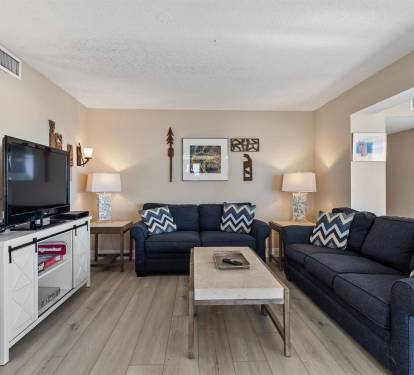 Unwind in your spacious living room with plush navy sofas, warm lighting, and entertainment center for cozy evenings together.