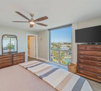 Your peaceful bedroom features rich wood furniture and a ceiling fan, with stunning views through floor-to-ceiling windows.