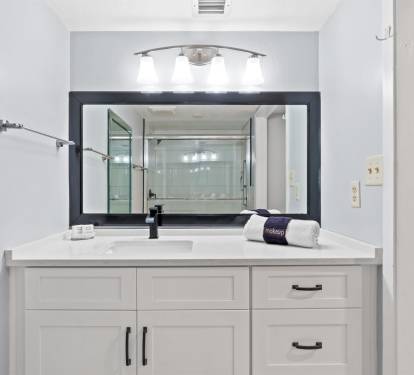 Your spacious bathroom features elegant white vanity with ample storage, modern lighting, and glass shower visible in the mirror reflection.