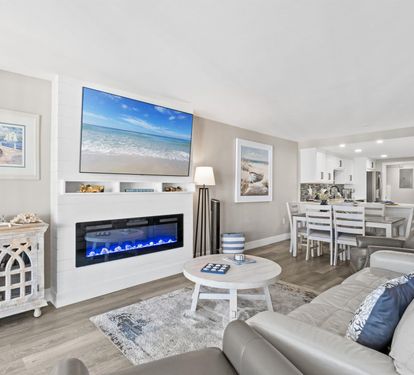 Relax in your sophisticated living area with coastal artwork, electric fireplace, and open kitchen perfect for memorable evenings together.