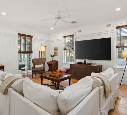 Unwind in this elegant living room with plush white sofas, warm hardwood floors, and modern entertainment setup for your perfect retreat.