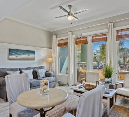 Stylish and sunlit 30A retreat with comfy seating, chic coastal décor, and floor-to-ceiling windows leading to a private balcony with palm views—ideal for relaxing in beachside comfort.