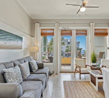 Cozy 30A living space with plush seating, beachy décor, and sunlit French doors leading to a balcony with tropical views—perfect for laid-back coastal living.