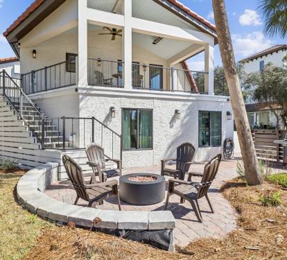 Modern coastal property featuring a ground-level patio with fire pit seating area, surrounded by palm trees and landscaped gardens.