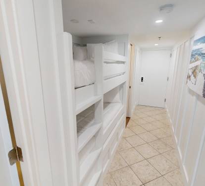 A bright hallway with built-in shelving and coastal artwork beckons you toward your tranquil beach retreat—perfect for storing all your vacation essentials while keeping the space light and airy.