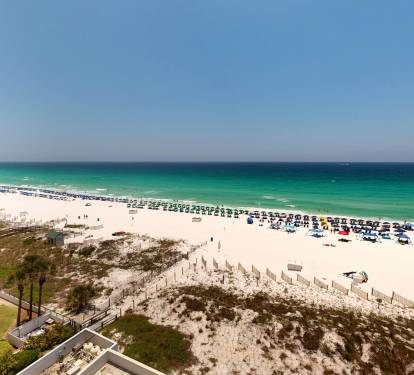 Wide panoramic view showcases the stunning white-sand beach, turquoise waters, and surrounding property amenities offering easy beach access and resort-style relaxation.