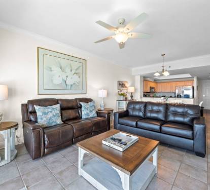 Relax in your spacious living room with comfortable leather seating, ceiling fan, and open concept design flowing into the full kitchen.