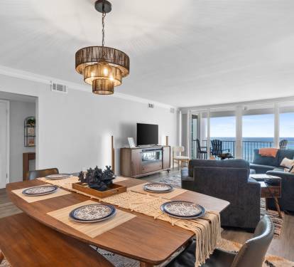 Your stylish oceanfront retreat features an open-plan living and dining space where warm wood accents meet stunning sea views through floor-to-ceiling windows.