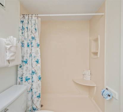 Step into your private bathroom with a spacious shower, fresh towels, and cheerful floral curtain for complete comfort.