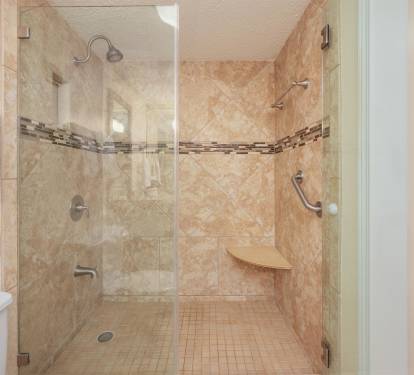 Step into your spacious walk-in shower with elegant travertine tiles, rainfall head, and convenient built-in seating for ultimate comfort.