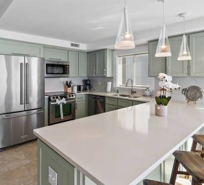 Your modern sage-green kitchen welcomes culinary adventures with gleaming countertops, stainless steel appliances, and pendant lights casting a warm glow over your island workspace.