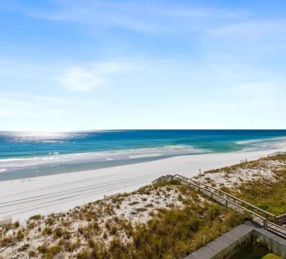 Pristine white sand beach stretches along turquoise waters with dunes and boardwalk access nearby.