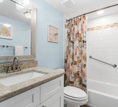 Refresh in your private bathroom featuring granite countertops, coastal artwork, and a relaxing tub-shower combo with charming seashell curtains.