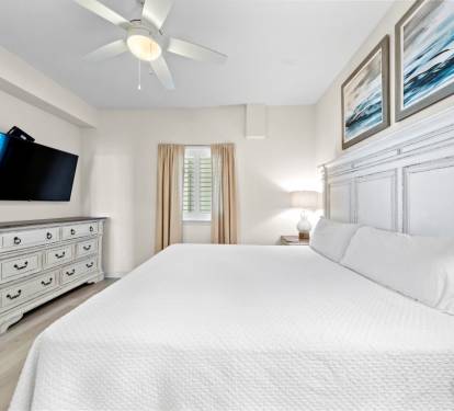 Drift off in this peaceful bedroom featuring crisp white linens, coastal artwork, and a gentle ceiling fan creating your perfect sleep sanctuary.