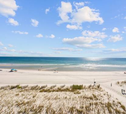 Pristine white sand beach stretches along turquoise waters under a brilliant blue sky dotted with fluffy white clouds.