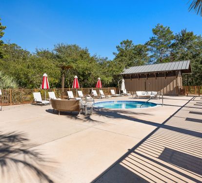 Pool deck surrounded by lush trees with comfortable lounge chairs, umbrellas, and tropical landscaping for ultimate relaxation.