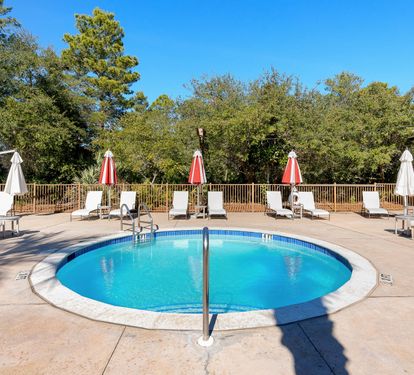 Sparkling outdoor pool surrounded by comfortable loungers and umbrellas, nestled in peaceful wooded surroundings for your perfect relaxation retreat.