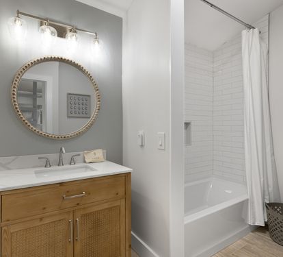 Step into your stylish bathroom featuring a warm wood vanity, elegant round mirror, and refreshing tub-shower combo for unwinding after adventures.