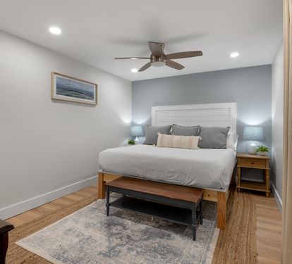 Relax in your cozy bedroom with comfortable bedding, peaceful coastal artwork, and gentle ceiling fan creating the perfect retreat.