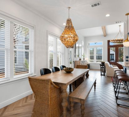 You'll love gathering around this stunning farmhouse table, bathed in natural light from oversized windows while the golden chandelier creates perfect ambiance.