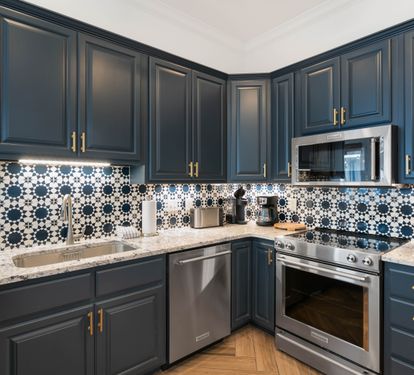 Your stylish kitchen features navy cabinetry, marble countertops, and stunning patterned tile backsplash, fully equipped for cooking memorable meals.