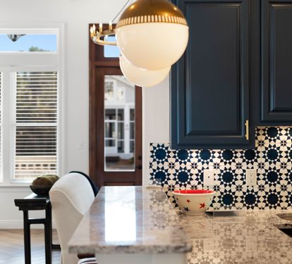 Your kitchen gleams with marble counters and striking navy cabinets, while patterned tiles add artistic flair to your culinary space.